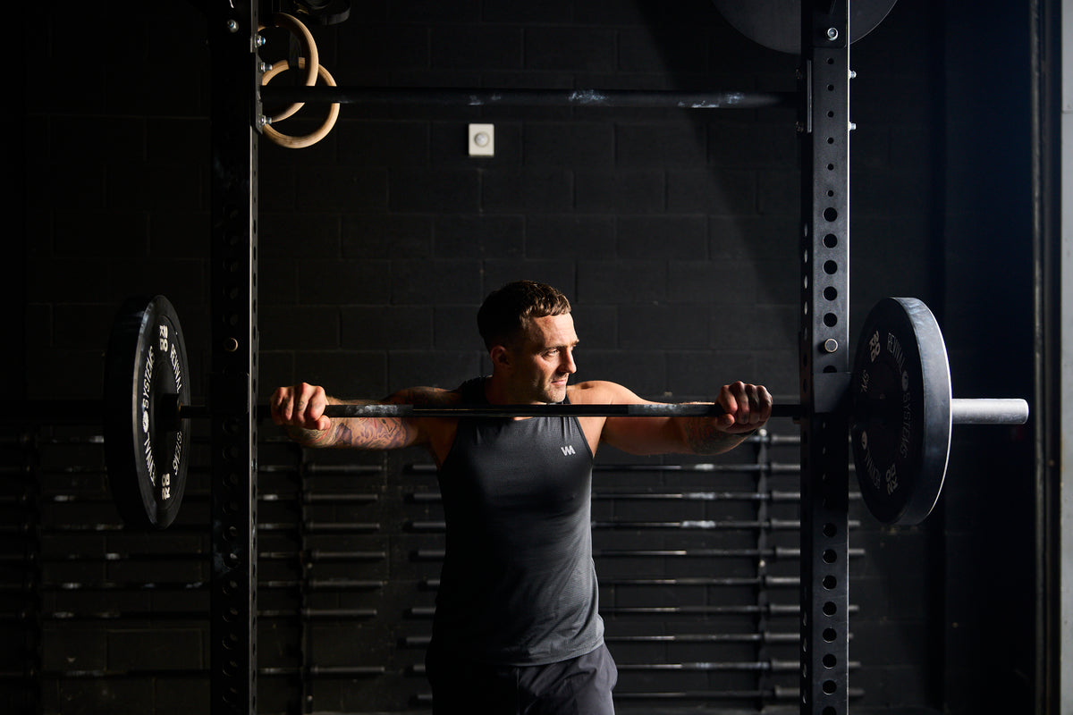 Man lifting a barbell in a gym setting with warrior additc branded clothing 