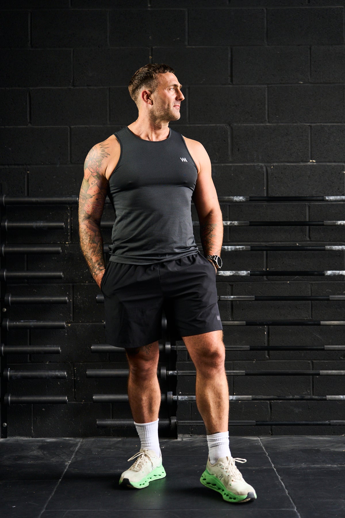 Man in black  warrior addict activewear standing against a black brick wall.