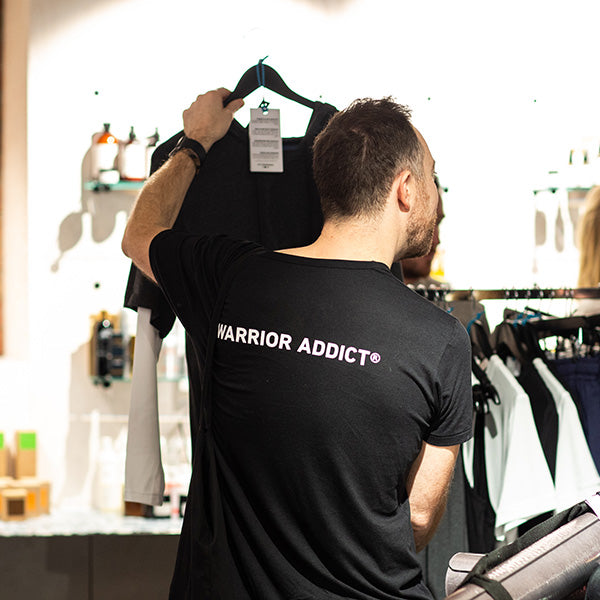 man with black warrior addict t-shirt on holding up a t-shirt in a shop