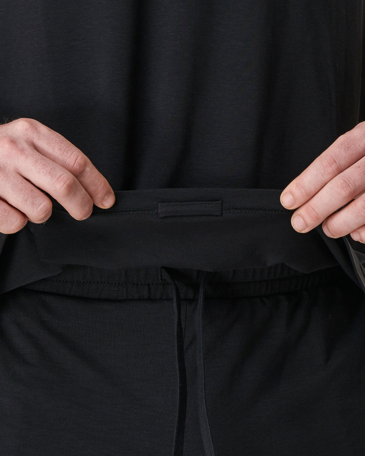 man showing hiddem loop inside seam of mens yoga top to stop the top from riding up 