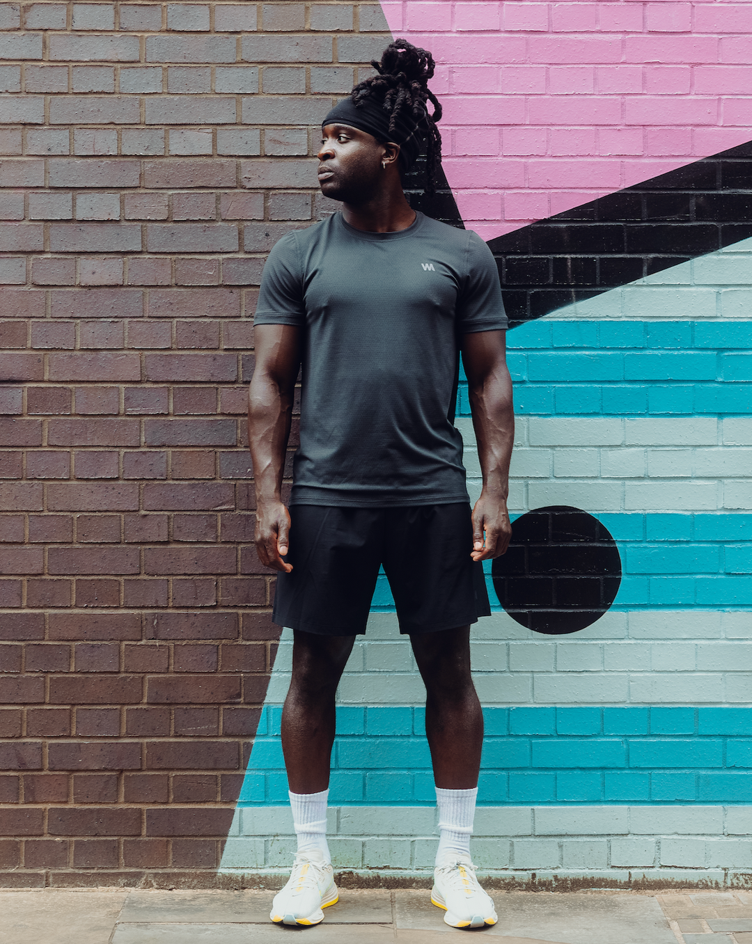 Man in Warrior Additc activwear standing in front of a colorful brick wall.