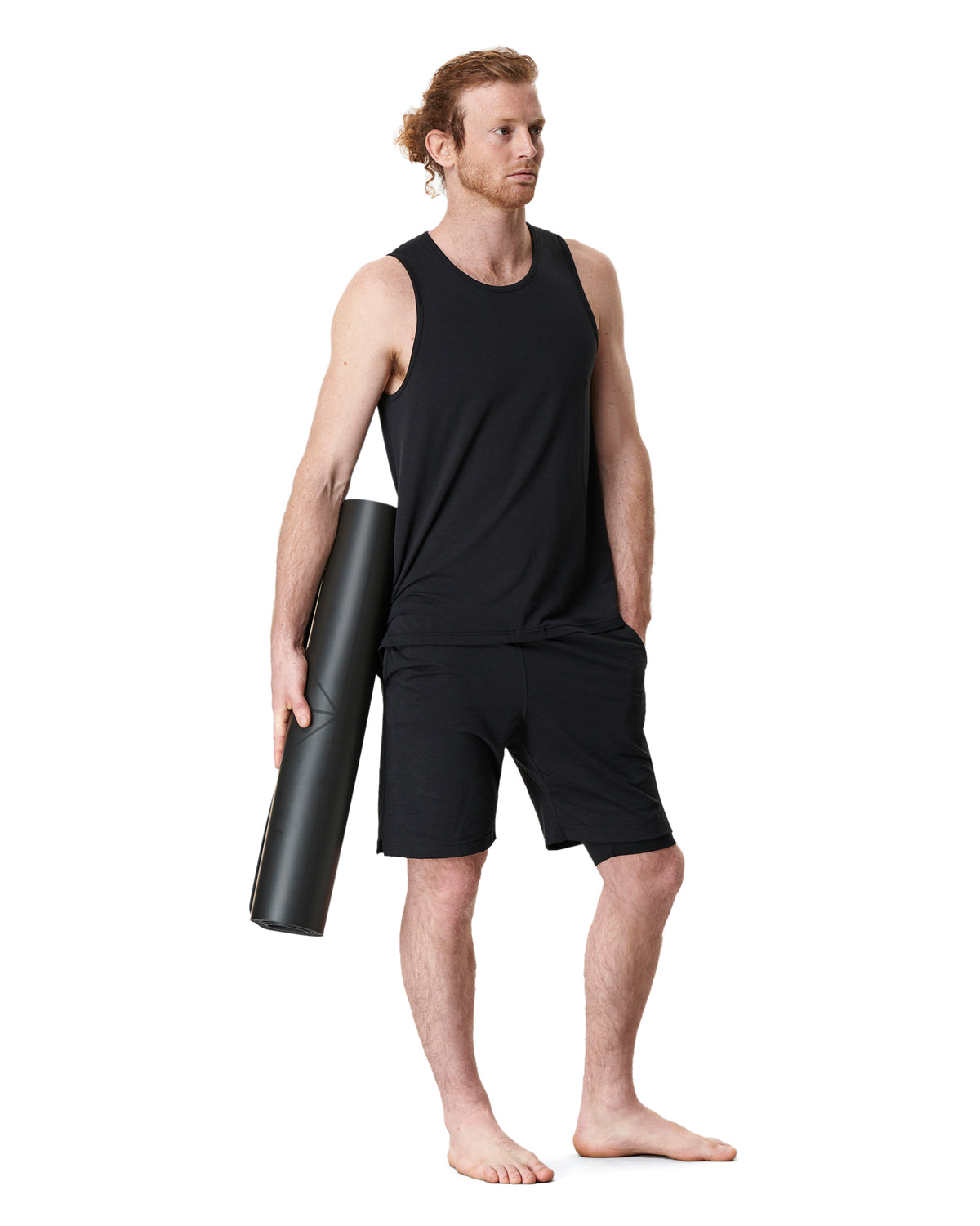 man wearing black yoga shorts and black yoga top and carrying a black mens yoga mat by warrior addict
