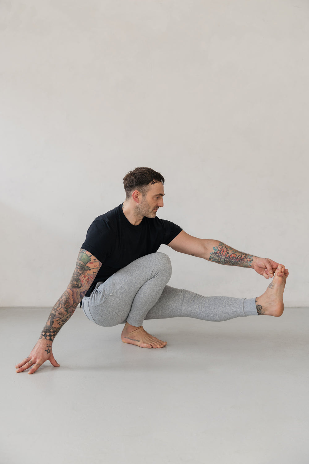 Man in yoga pose wearing black t-shirt and gray sweatpants.