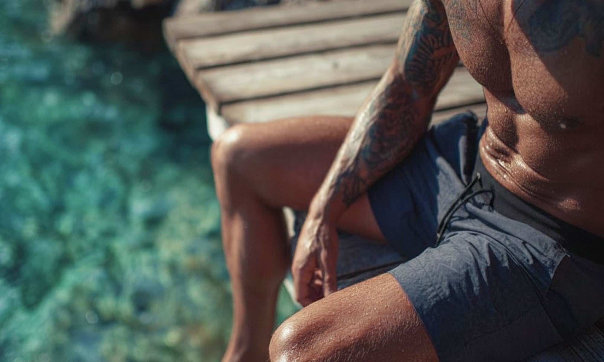 Person sitting by the sea on a deck with tattooed arm and grey warrior addict activwear shorts 
