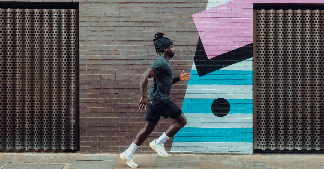 Man  in Warrior Addict's running clothes running in front of a colorful geometric mural on a wall.