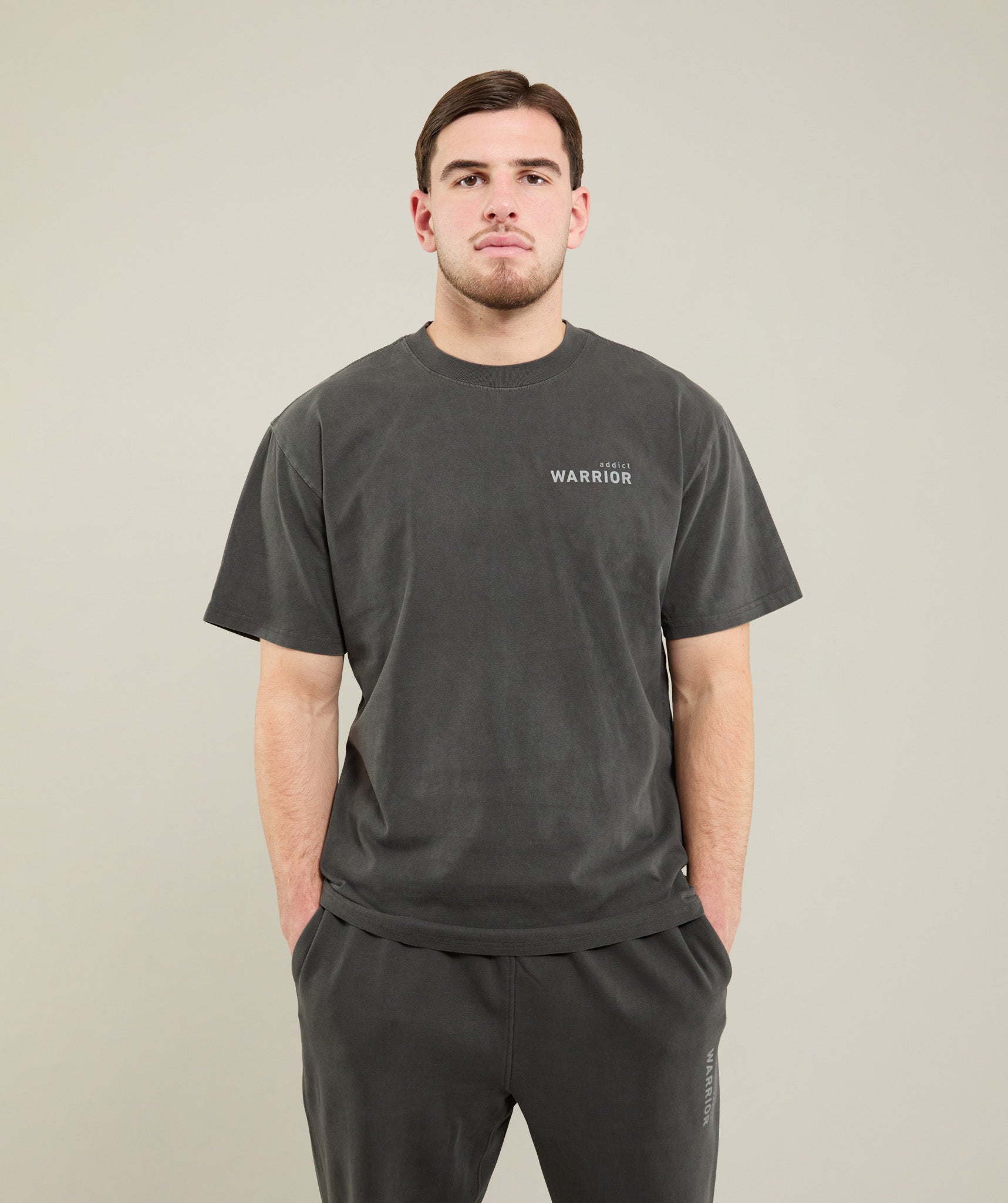 Man wearing a faded black t-shirt and pants  with warrior addict logo on a plain background