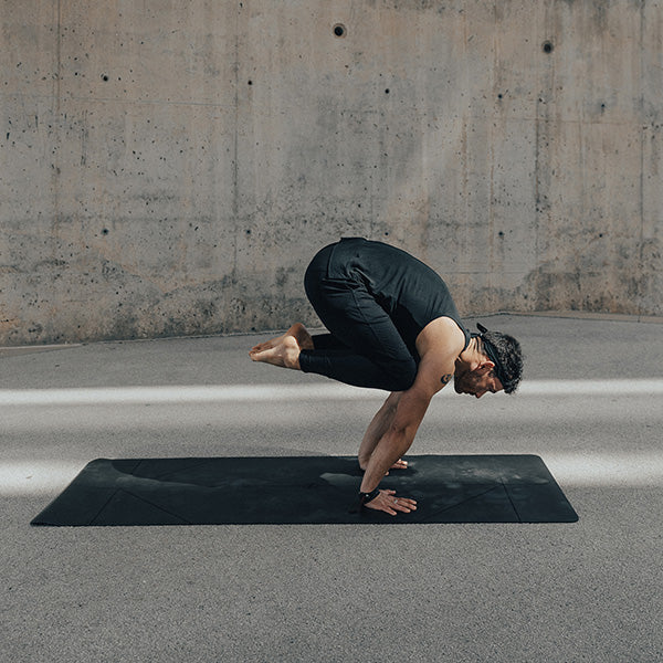 Man practicing an arm balance on a black warrior addict yoga mat 