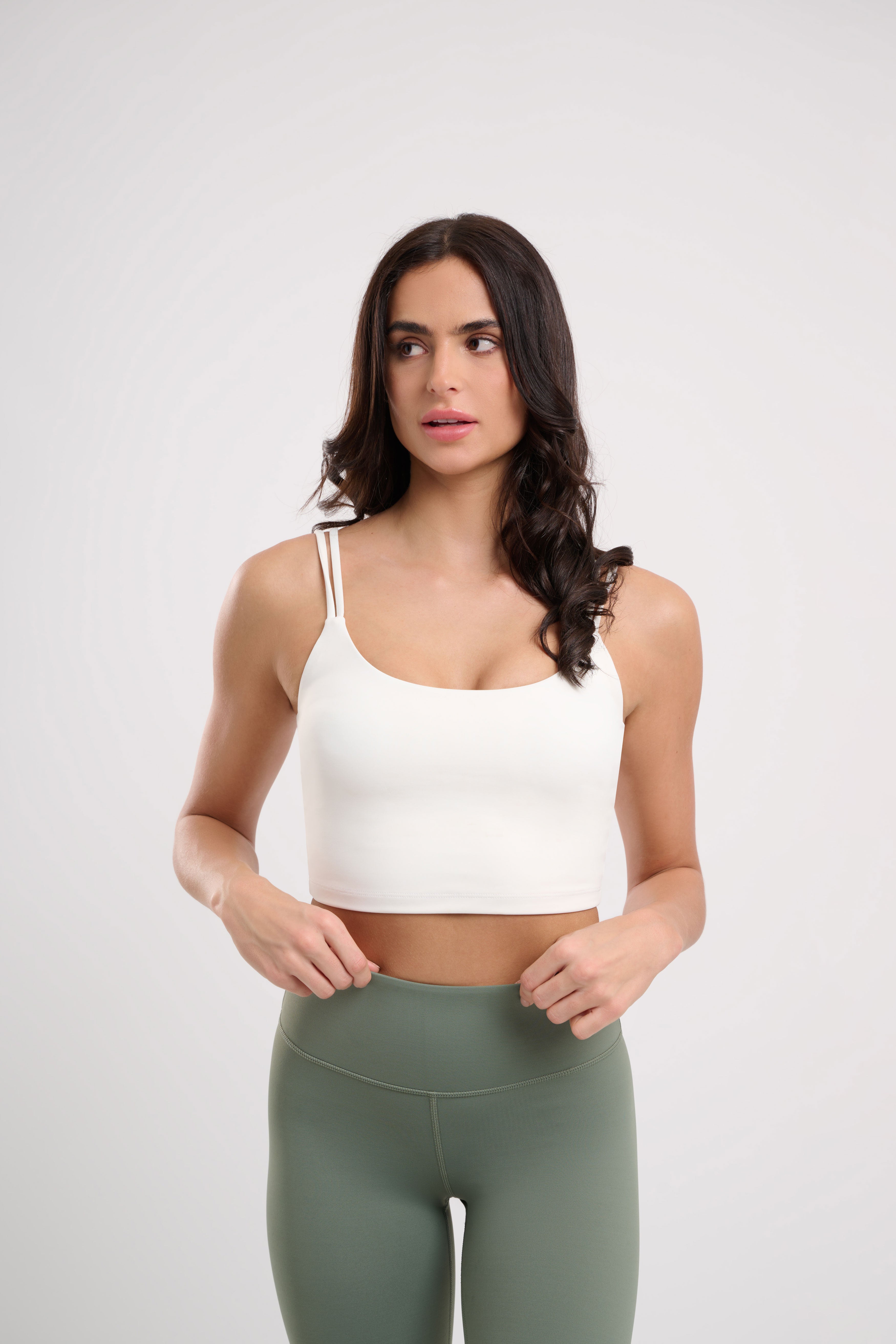 Woman in a white tank top and green leggings, standing.