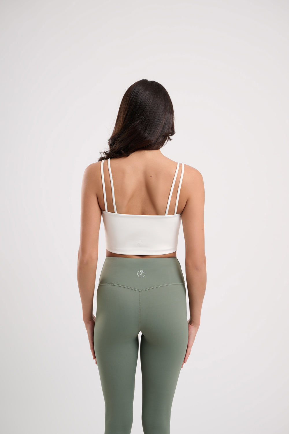 Woman in white crop top and green leggings, back view.
